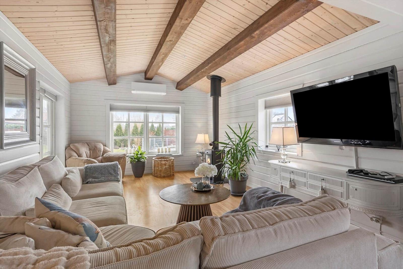 Wohnzimmer mit Holzdecke, Sofa, Fernseher und Kaminofen.