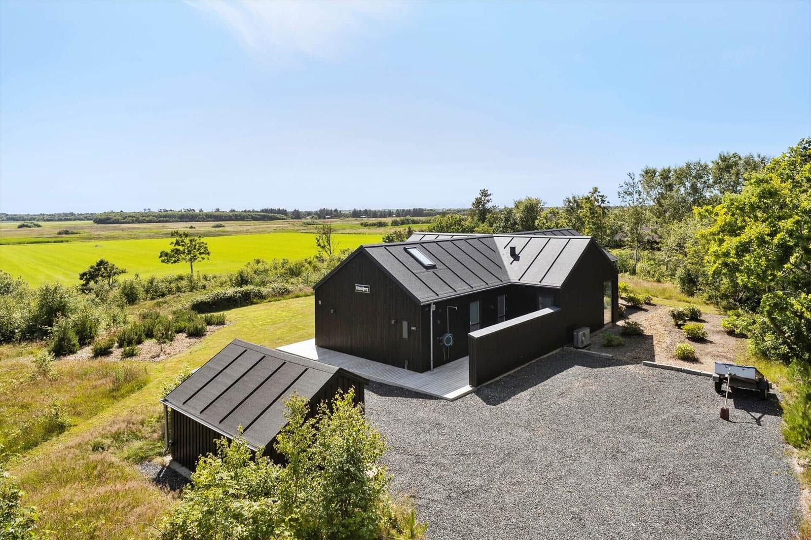 Moderne schwarze Hütte mit Garten und Blick auf grüne Felder.