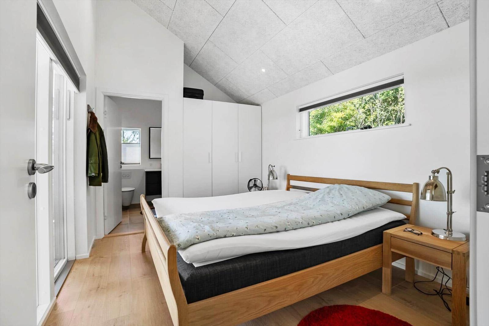 Schlafzimmer mit Bett, Schrank und Fenster. Badezimmer im Hintergrund.