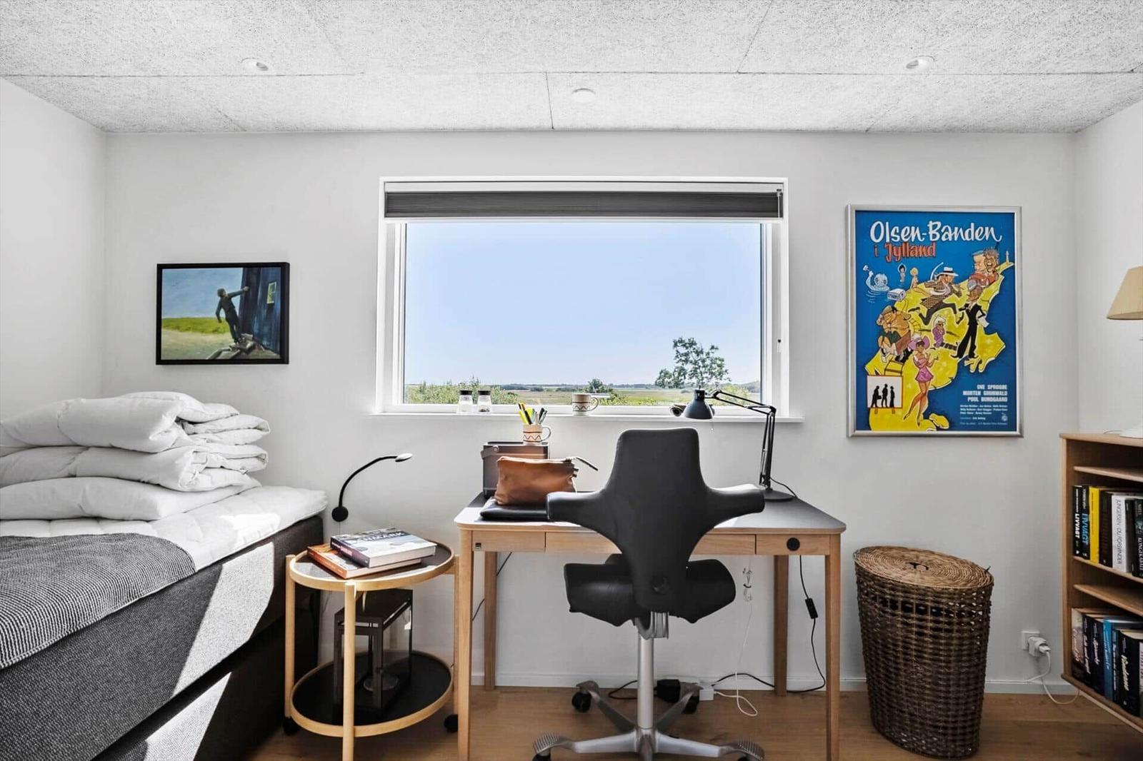 Zimmer mit Bett, Schreibtisch, Stuhl und Fenster mit Blick auf Landschaft.