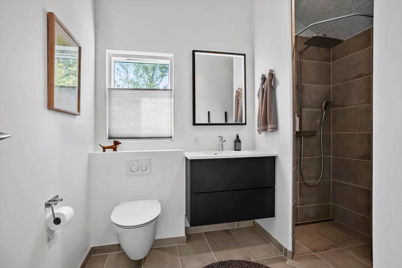 Badezimmer mit Dusche, Waschbecken und Toilette. Fenster mit Jalousie.