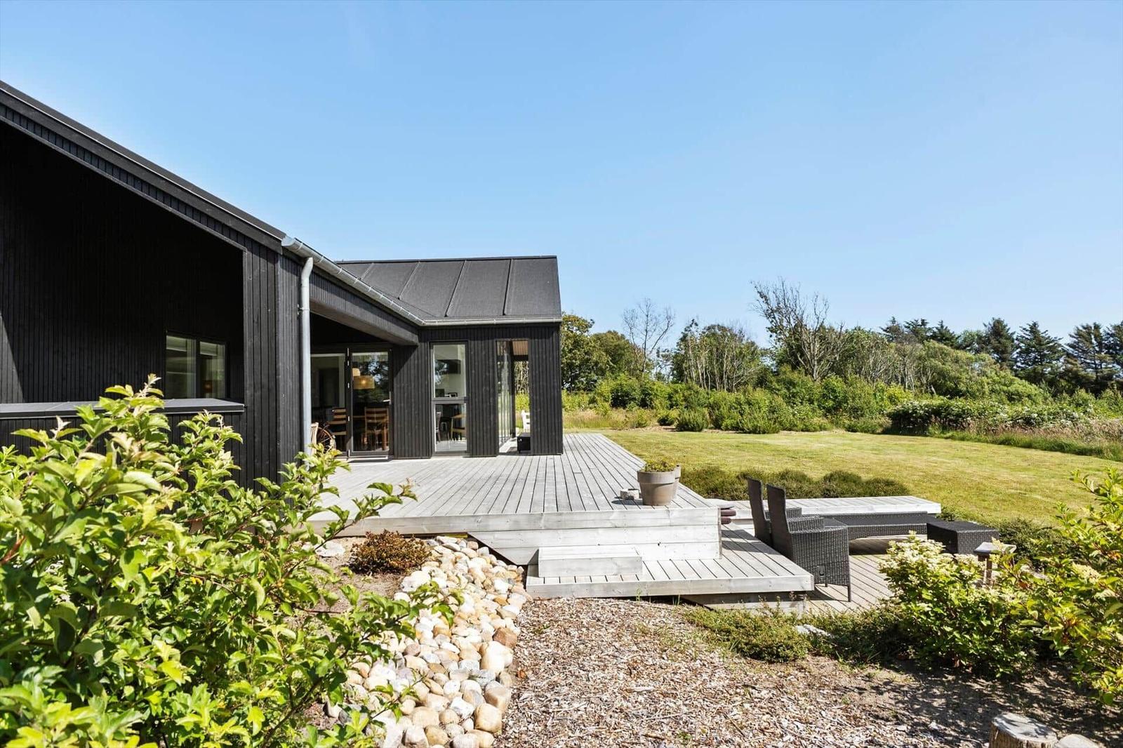 Moderne Villa mit Terrasse und Garten. Große Fenster und schwarze Fassade.