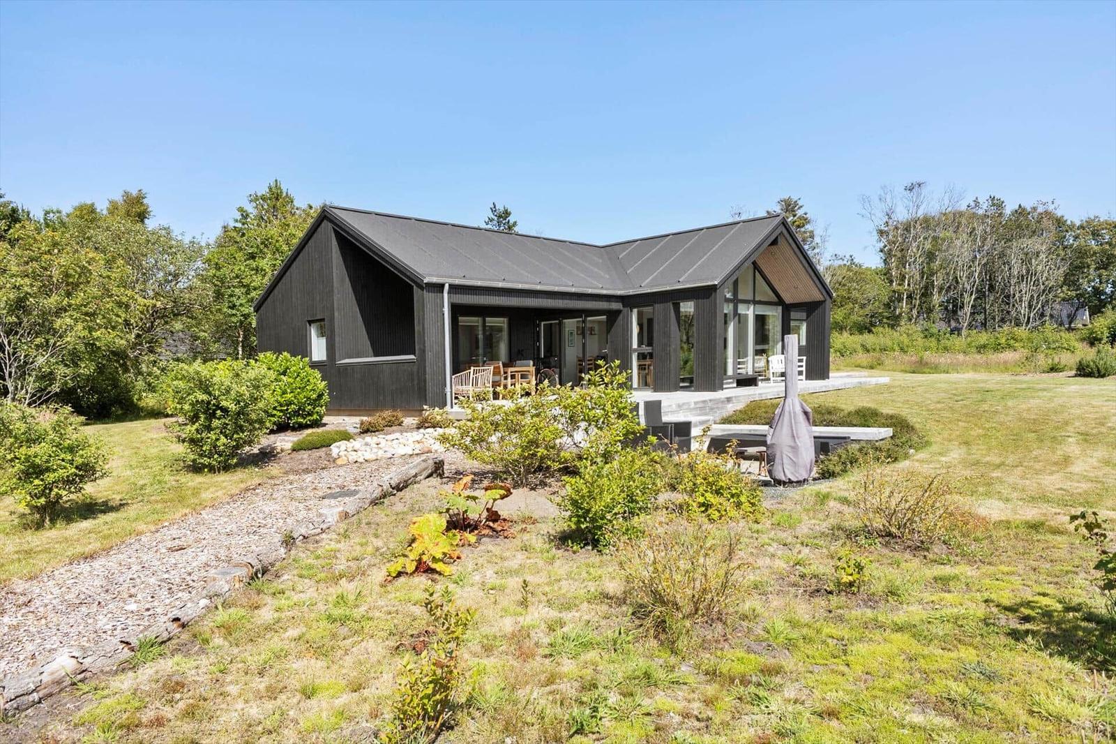 Moderne Villa mit großem Garten und Terrasse. Holz- und Glasfassade. Grünflächen und Bäume umgeben das Haus.