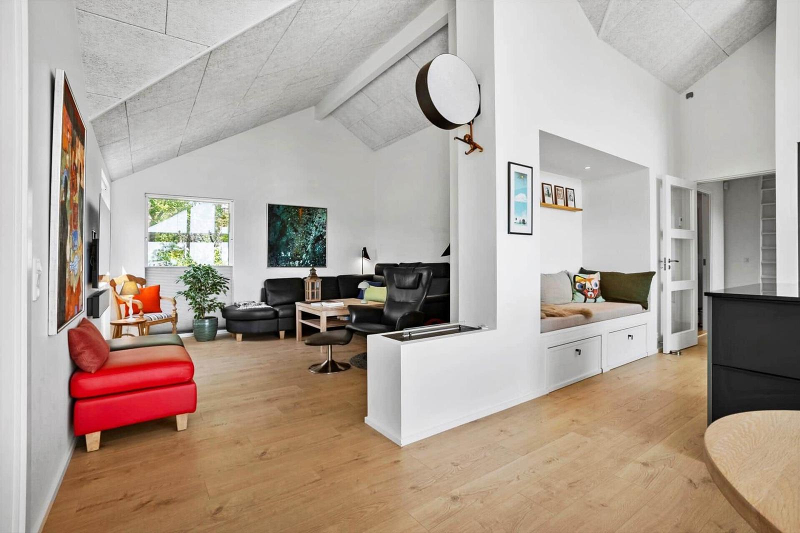 Wohnraum mit rotem Sessel, schwarzer Couch und Holzboden.