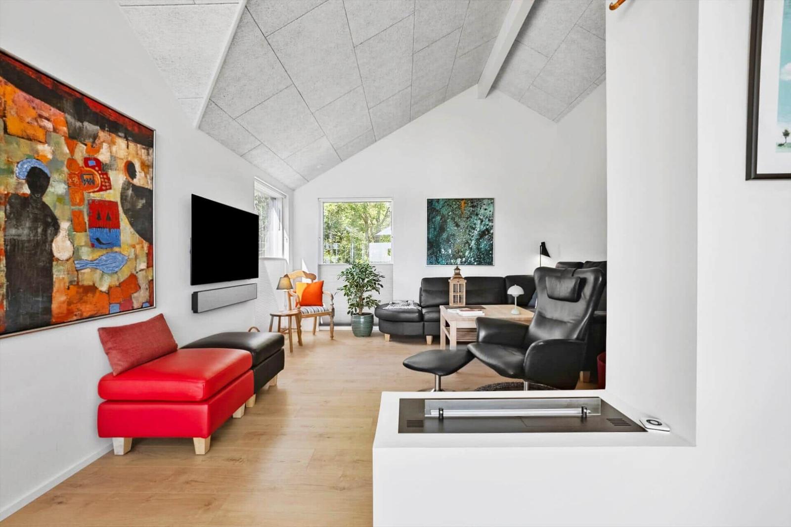 Wohnzimmer mit rotem Sitzmöbel, schwarzen Ledersofas und Fernseher an der Wand.
