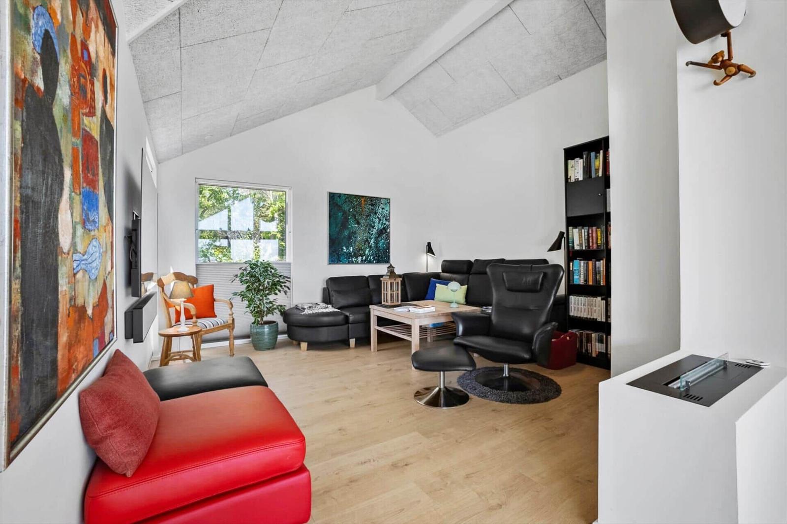 Wohnzimmer mit rotem Sofa, schwarzen Sesseln und Holzboden. An der Wand hängt ein großes Bild.