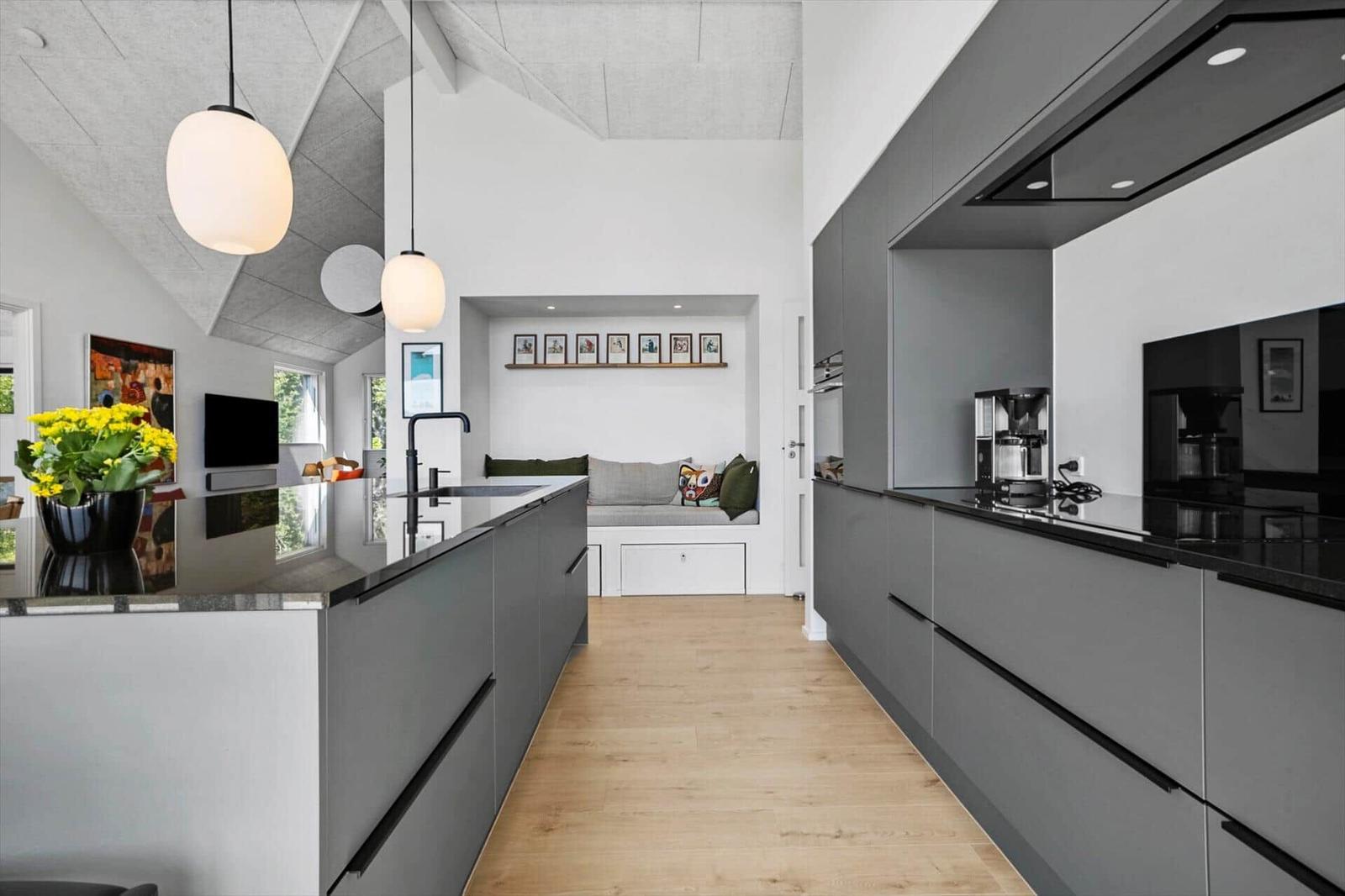 Moderne Küche mit grauen Schränken und Holzboden. Sitznische mit Kissen und Bildern an der Wand.