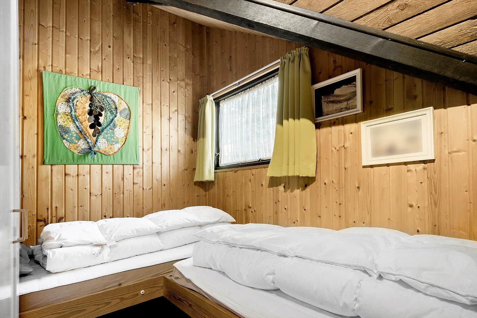 Zwei Betten mit weißen Laken in einem Holzhaus mit Fenster und Wanddekoration.
