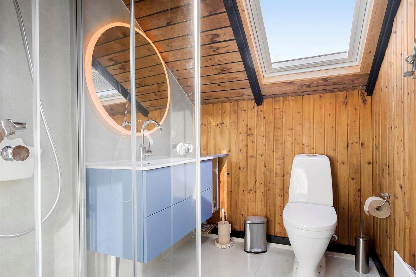 Badezimmer mit Dusche, Waschbecken und Toilette unter Holzdecke mit Dachfenster.