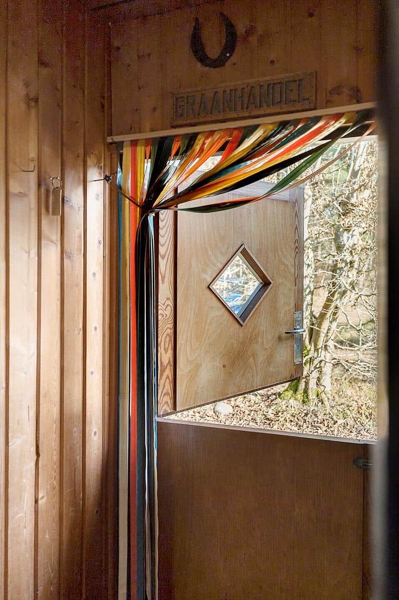Holztür mit Diamantfenster und bunten Bändern, darüber Schild mit Schmiedehammer.