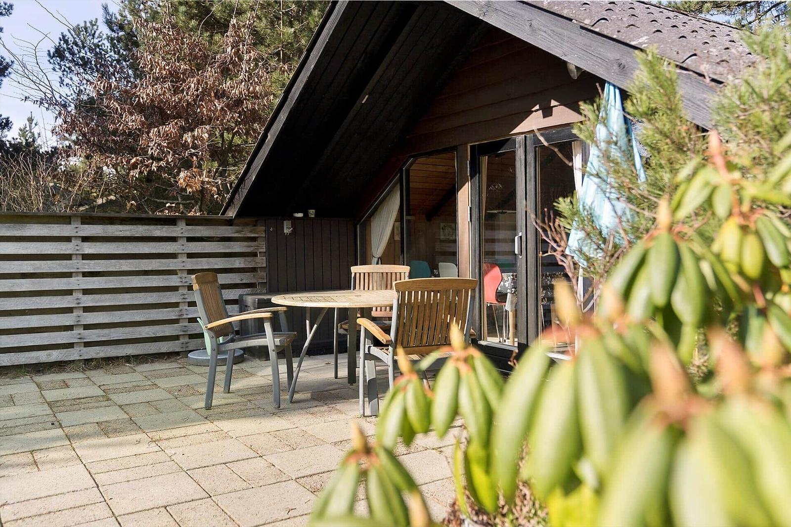 Terrasse mit Tisch und Stühlen vor einem Holzhaus mit Glasfront.