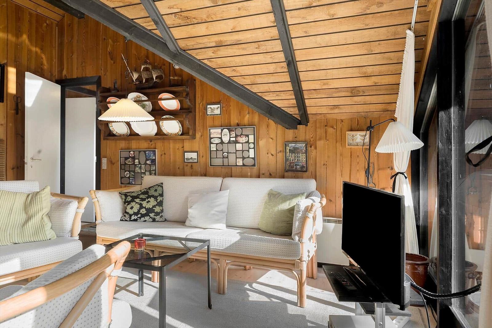 Wohnzimmer mit Holzwand, Sofa, Fernseher und Glas-Tisch.
