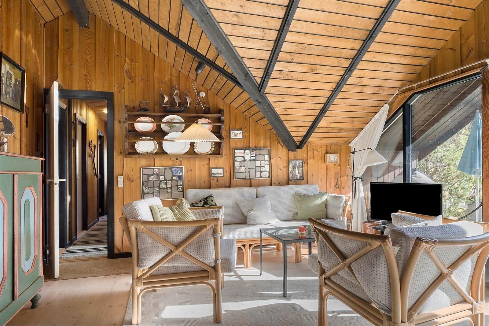 Wohnzimmer mit Holzwand, Sofa, zwei Stühlen und Glas-Tisch. Decke mit Holz und Metallträgern.