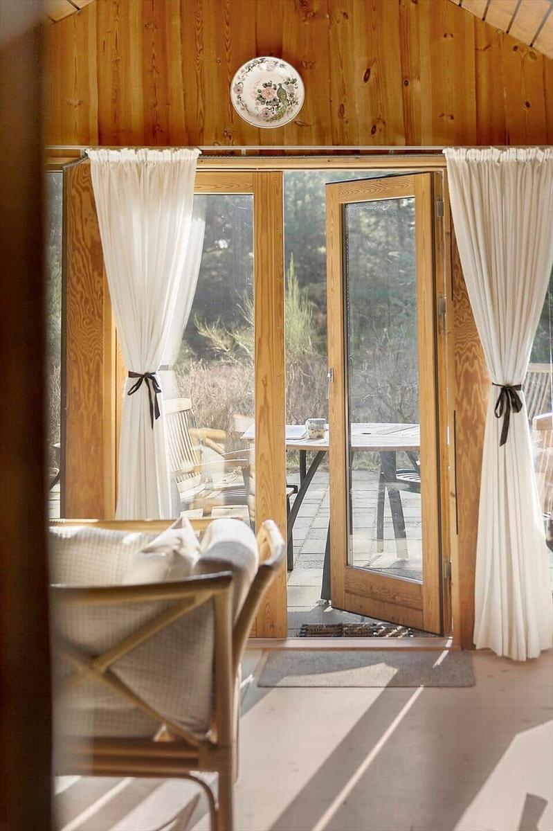 Holzgetäfeltes Interieur mit Glastüren zum Balkon. Weiße Vorhänge und hölzerner Stuhl.