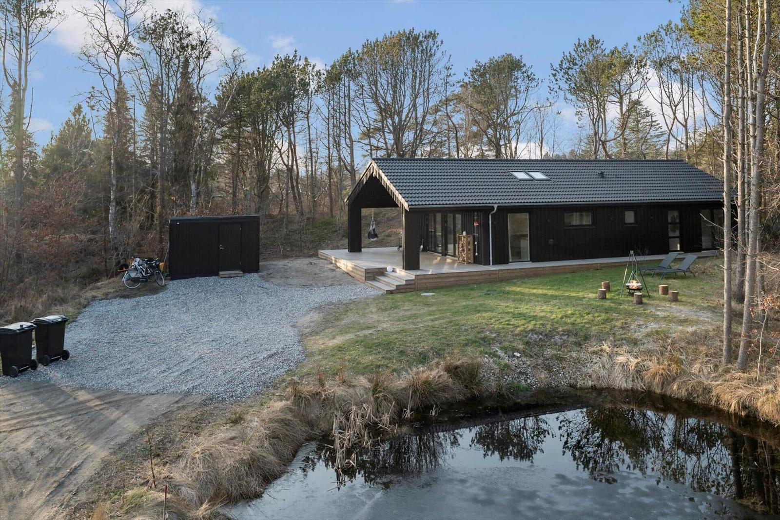 Modern cabin with terrace, garden, and small pond in the woods