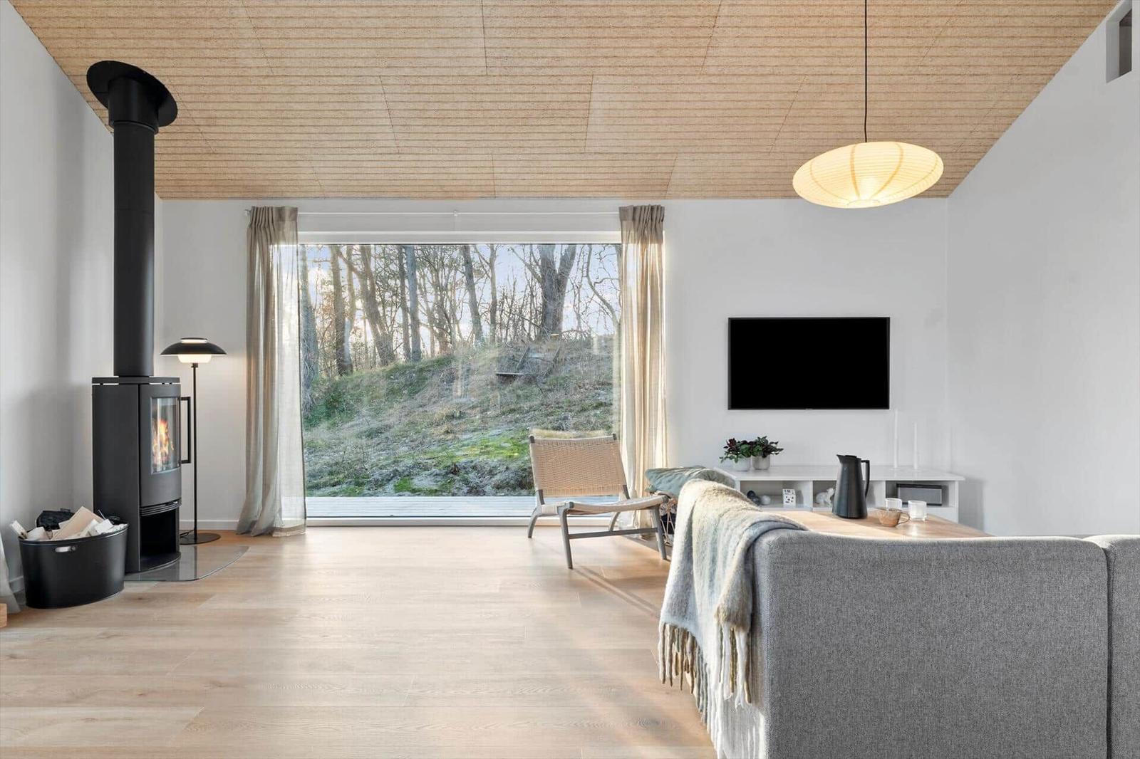Living room with fireplace, large window, and sofa. Wooden ceiling and light walls.