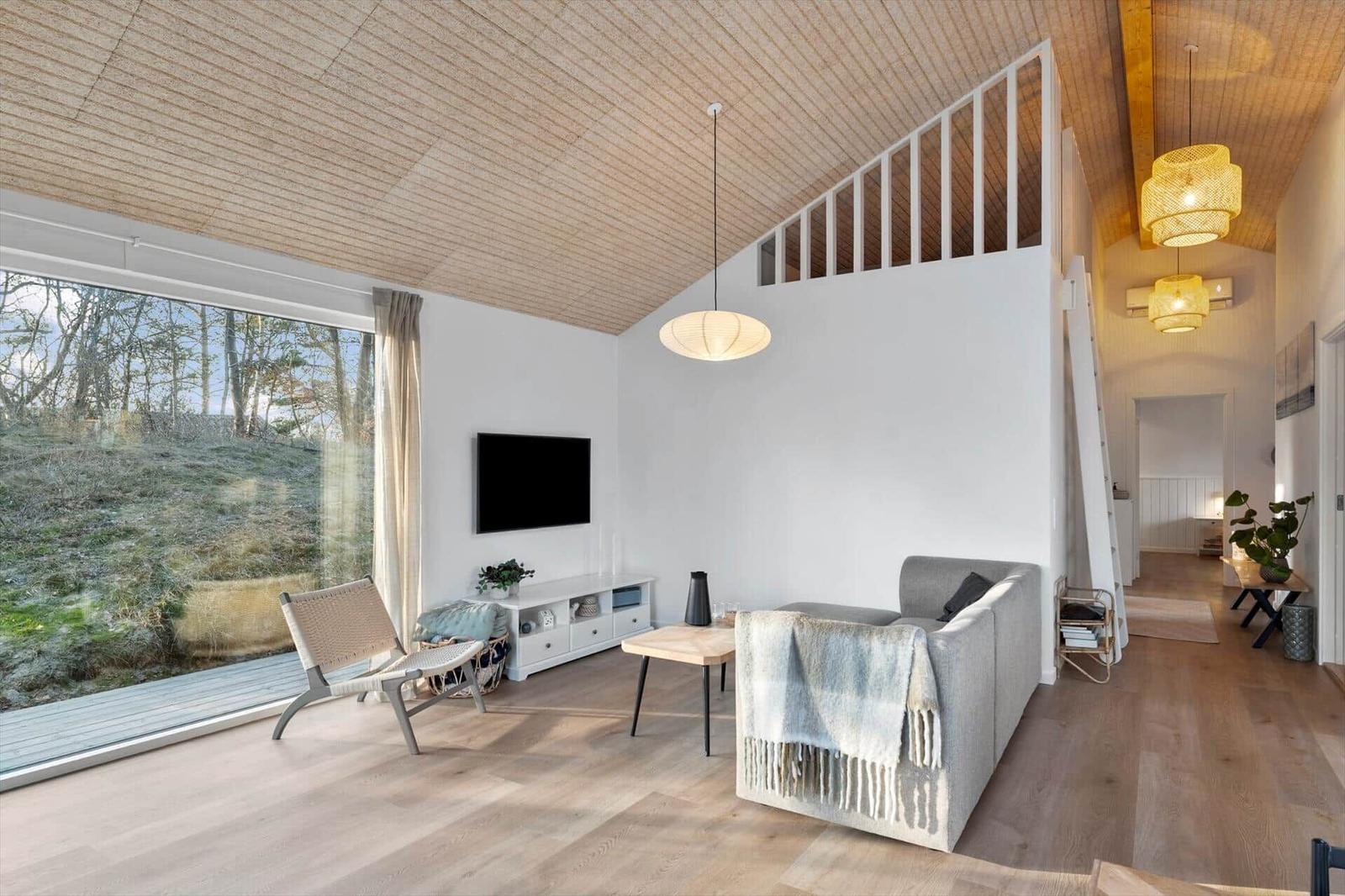 Living room with wooden ceiling, sofa, TV, and large window to nature.