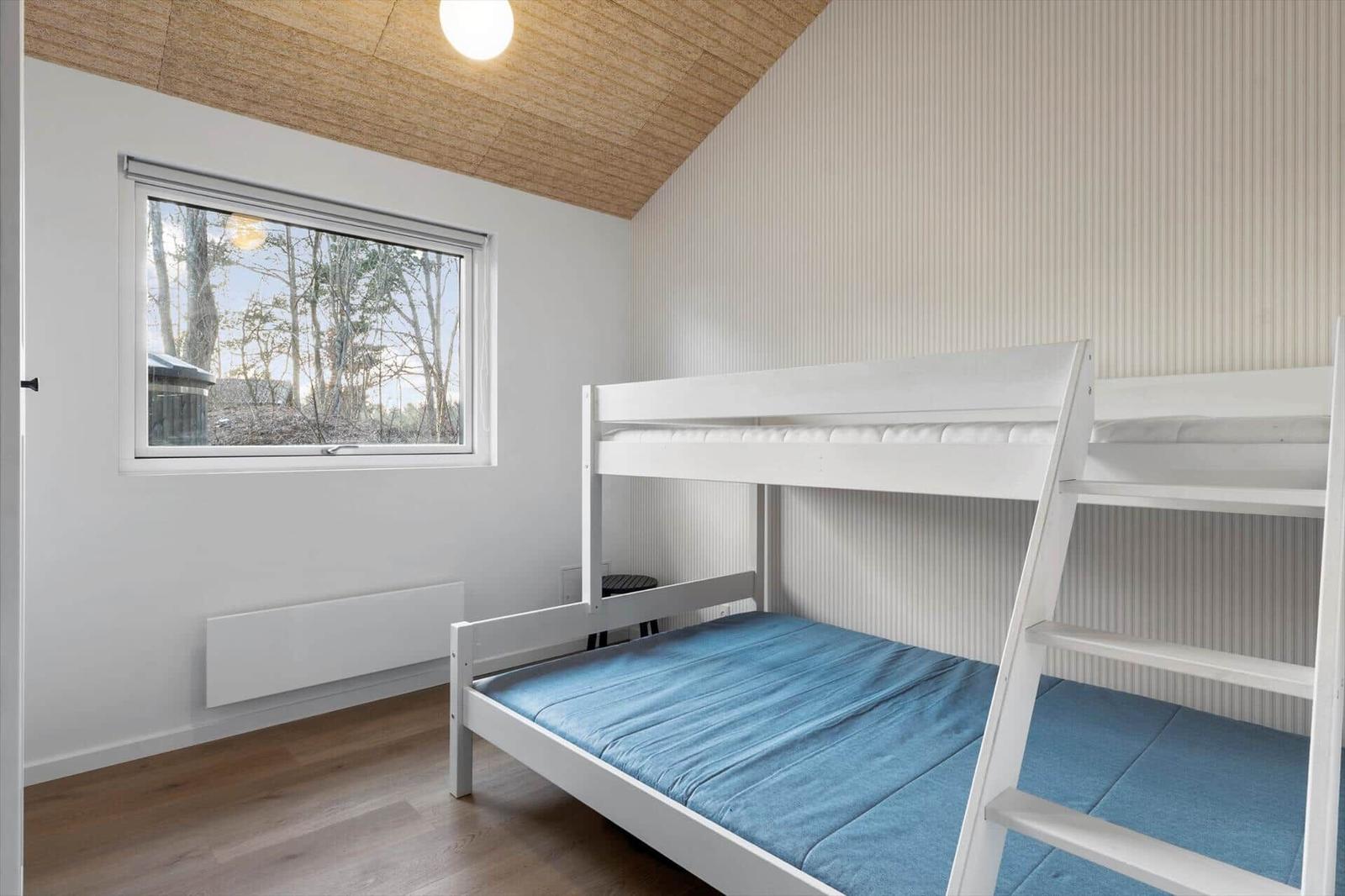Room with bunk bed, wooden floor, and window with forest view.