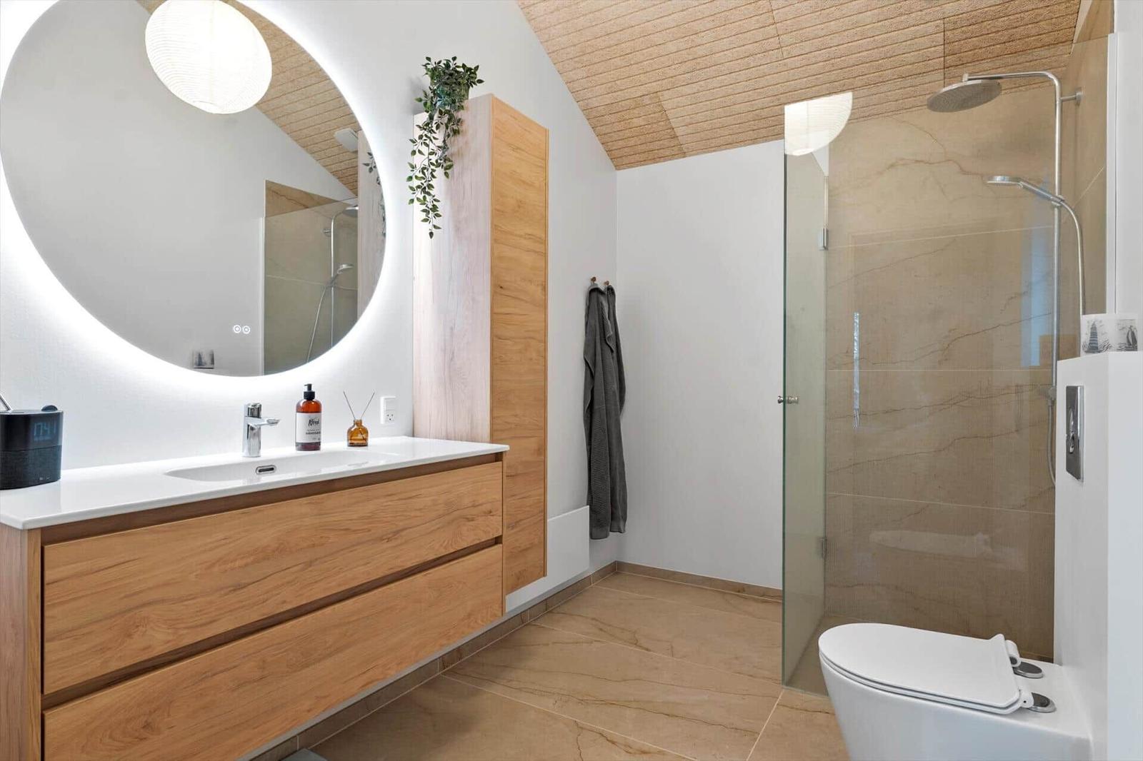 Bathroom with sink, shower, and toilet. Wood and stone look.