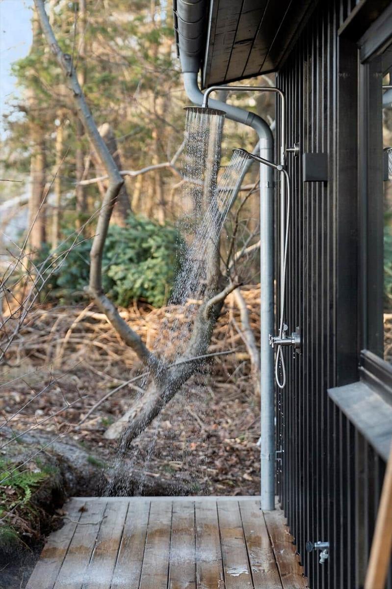 Outdoor shower at modern wooden cabin with forest in background.