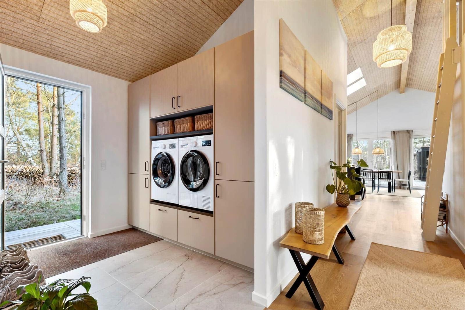 Washroom with integrated washing machines and wooden shelves. View of the forest through the door.