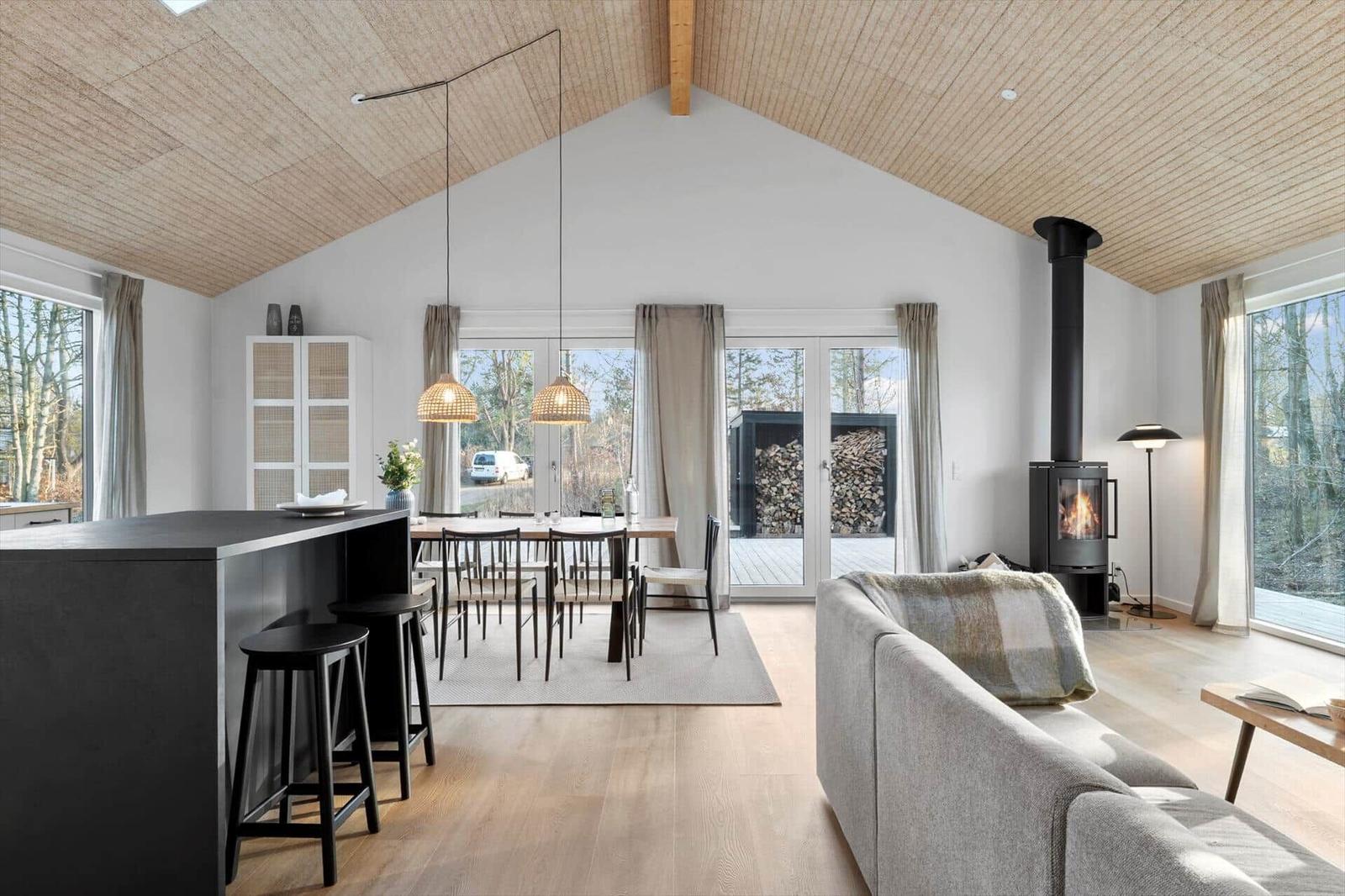 Living and dining area with fireplace, large windows, and wooden ceiling.