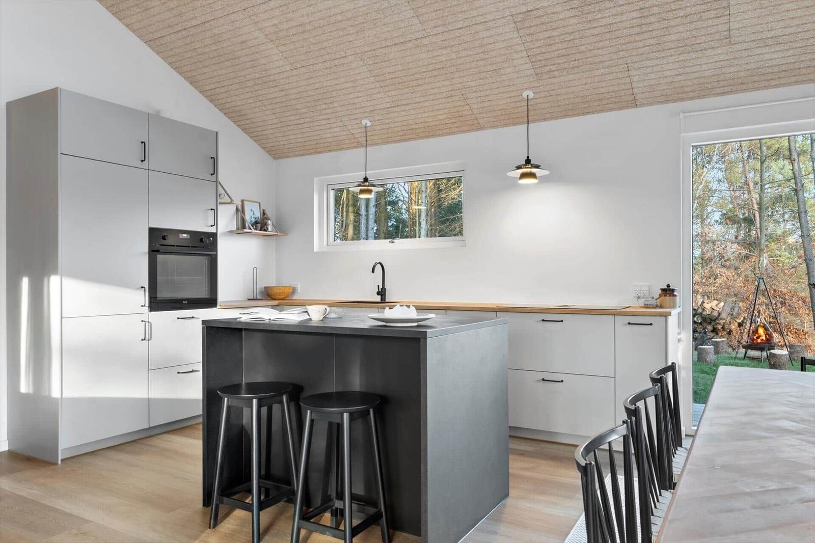 Modern kitchen with island, wooden ceiling, and view of the garden.