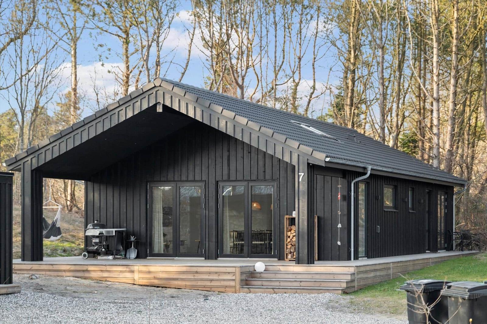 Modern black cabin with wooden terrace and grill in the woods