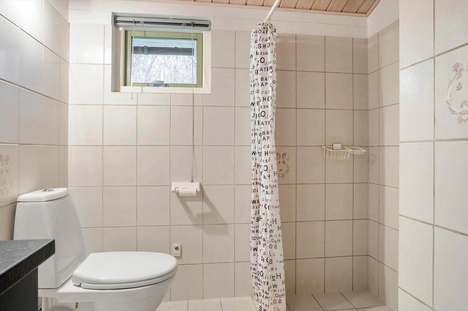Badezimmer mit Toilette, Dusche und kleinem Fenster.