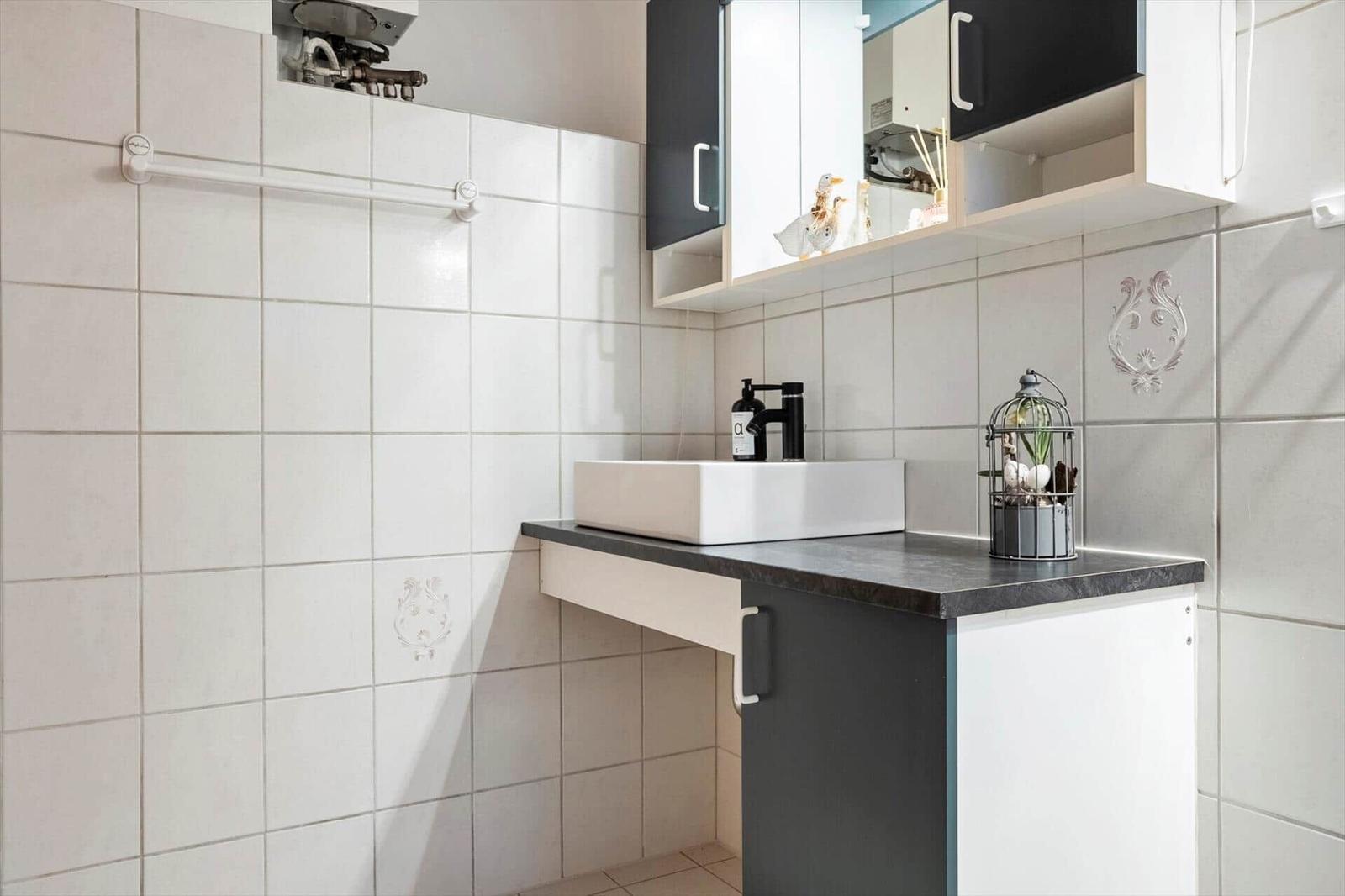 Badezimmer mit Waschbecken, Schrank und Handtuchhalter an Wand.