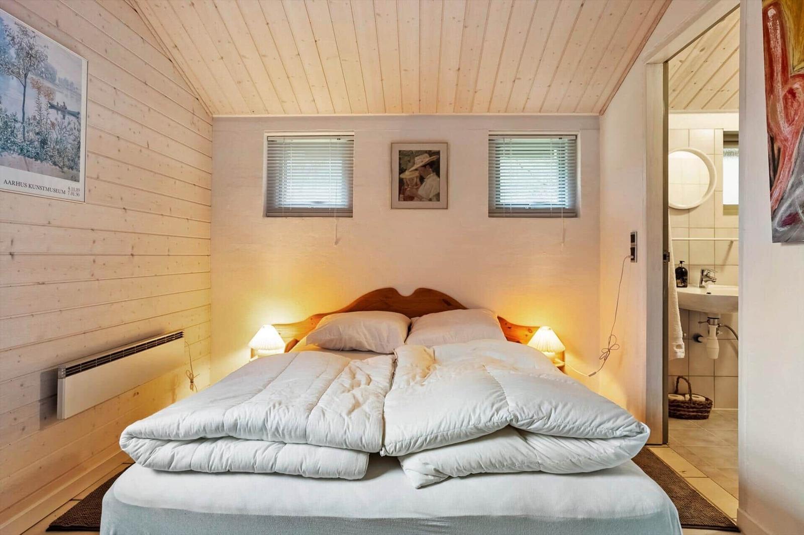 Schlafzimmer mit Bett, zwei Fenstern und angrenzender Toilette.