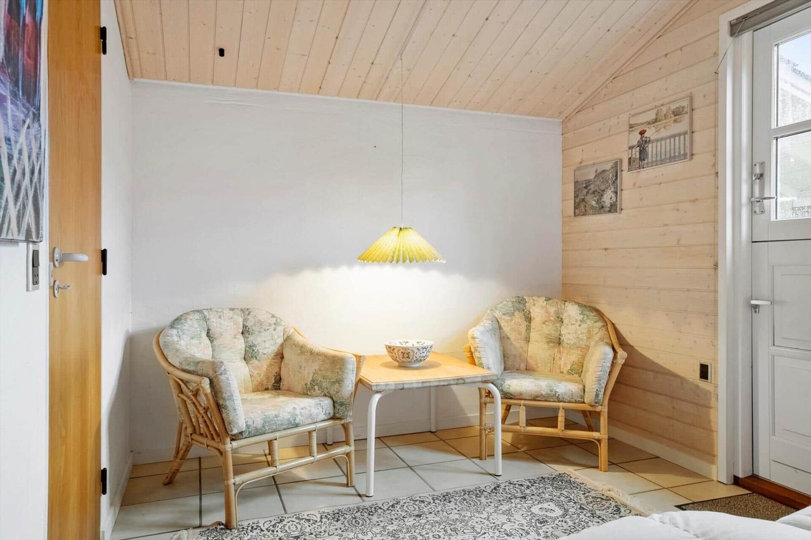 Zwei Stühle und ein Tisch unter einer Lampe in einem Raum mit Holzwand und -decke.