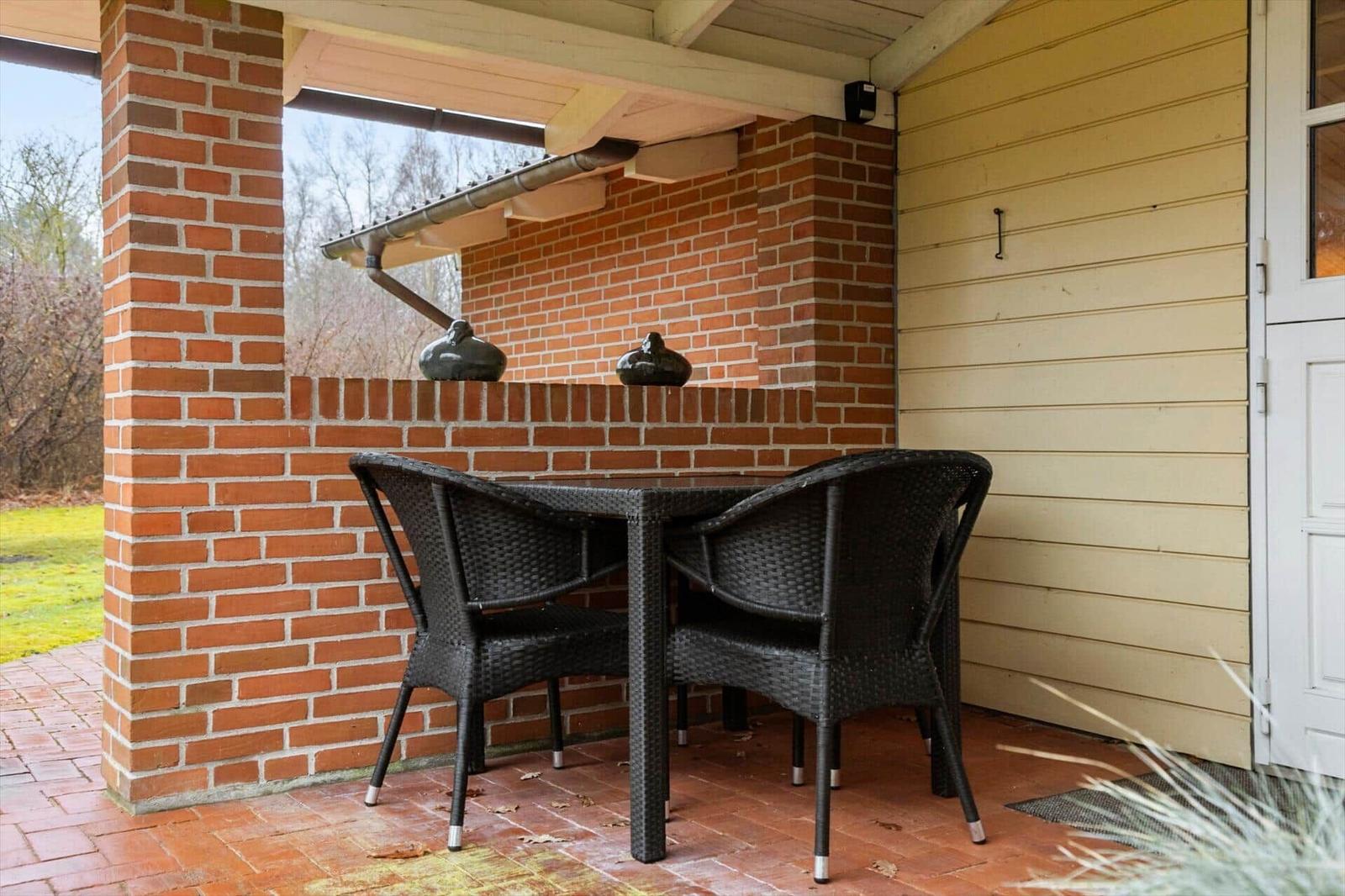 Terrasse mit Tisch und zwei Stühlen, rote Ziegelwand und Holzverkleidung.