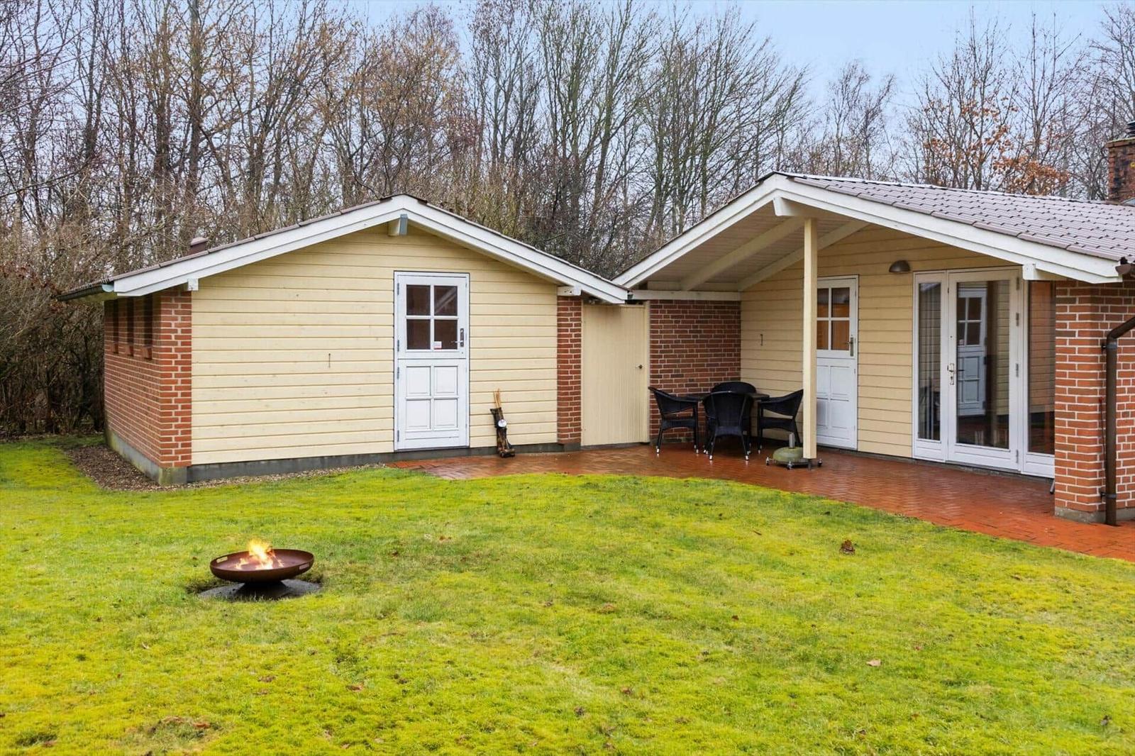 Haus mit Terrasse, Garten und Feuerkorb. Hintergrund: Wald.