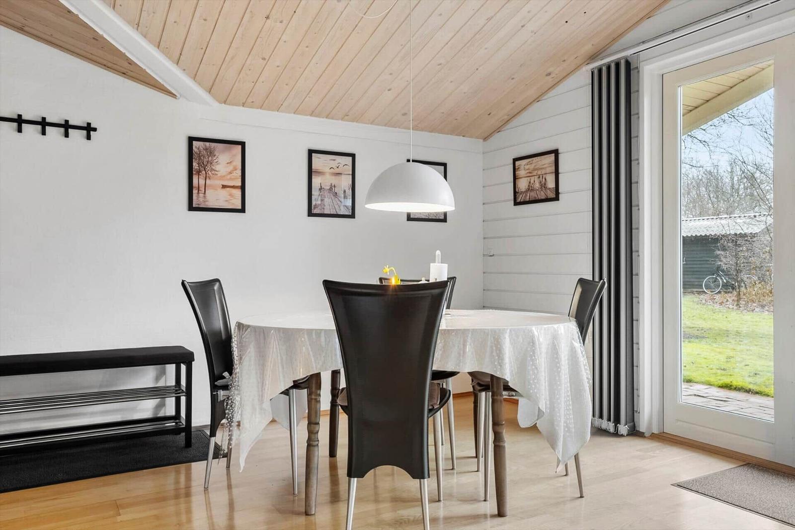 Esszimmer mit runden Tisch, schwarzen Stühlen und Holzdecke. Durchgang zur Außenterrasse.