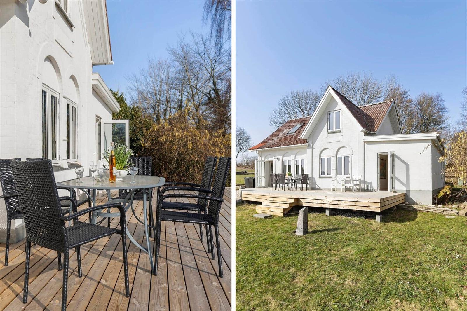 White house with terrace and garden. Table and chairs on wooden terrace.