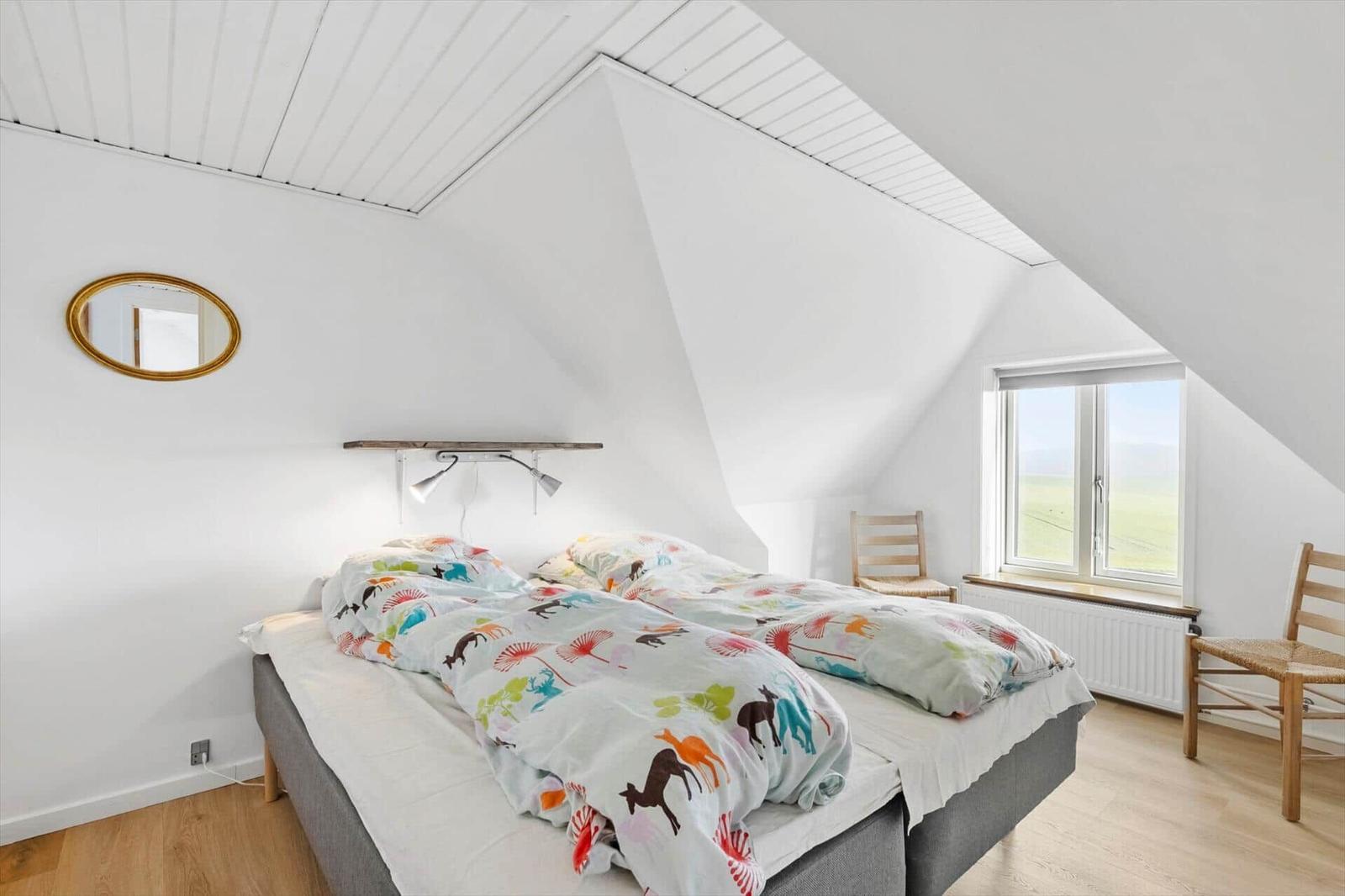 Bedroom with sloped ceiling, bed, window, and two chairs.