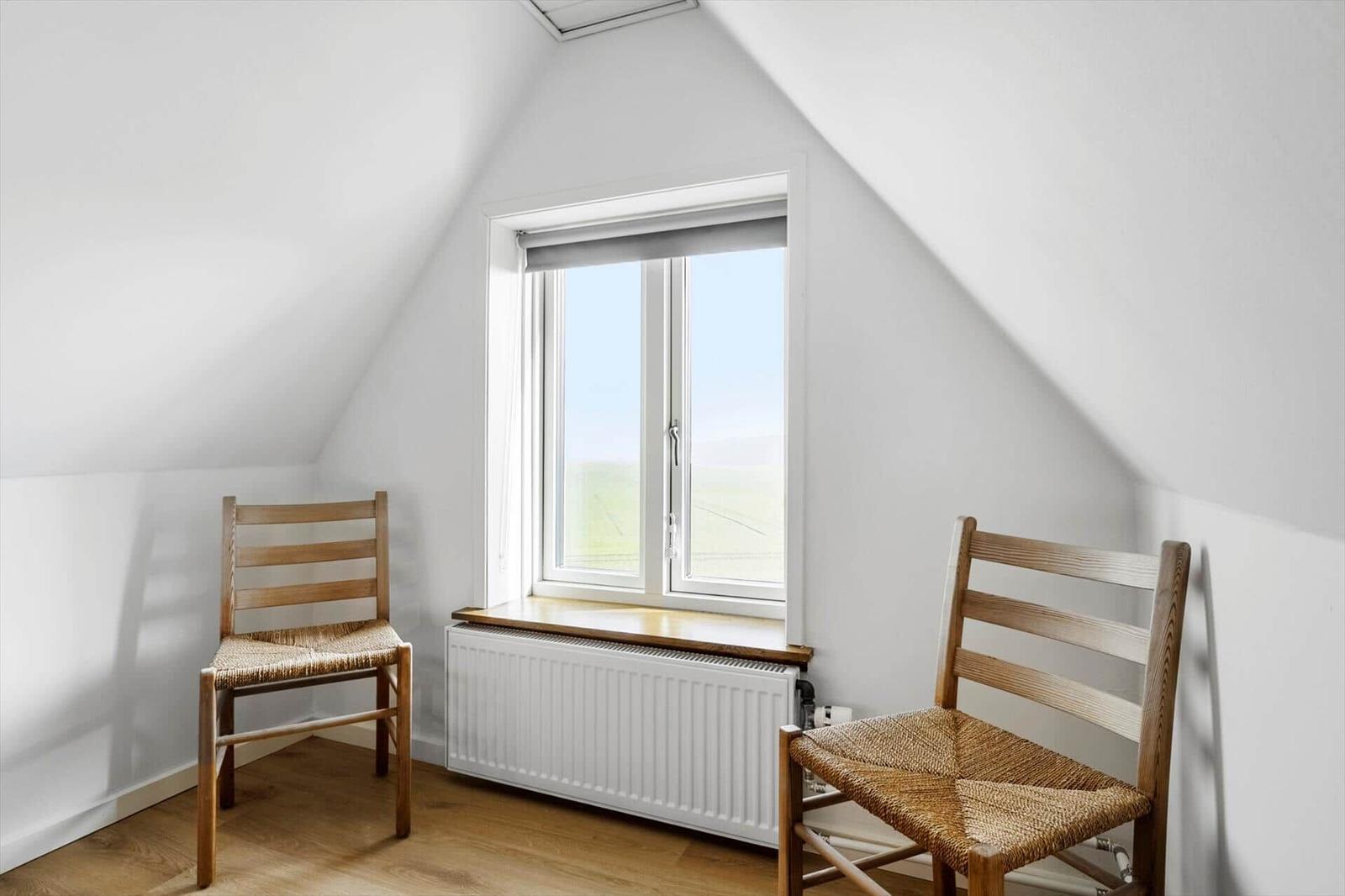Room with two wooden chairs, window, and radiator.