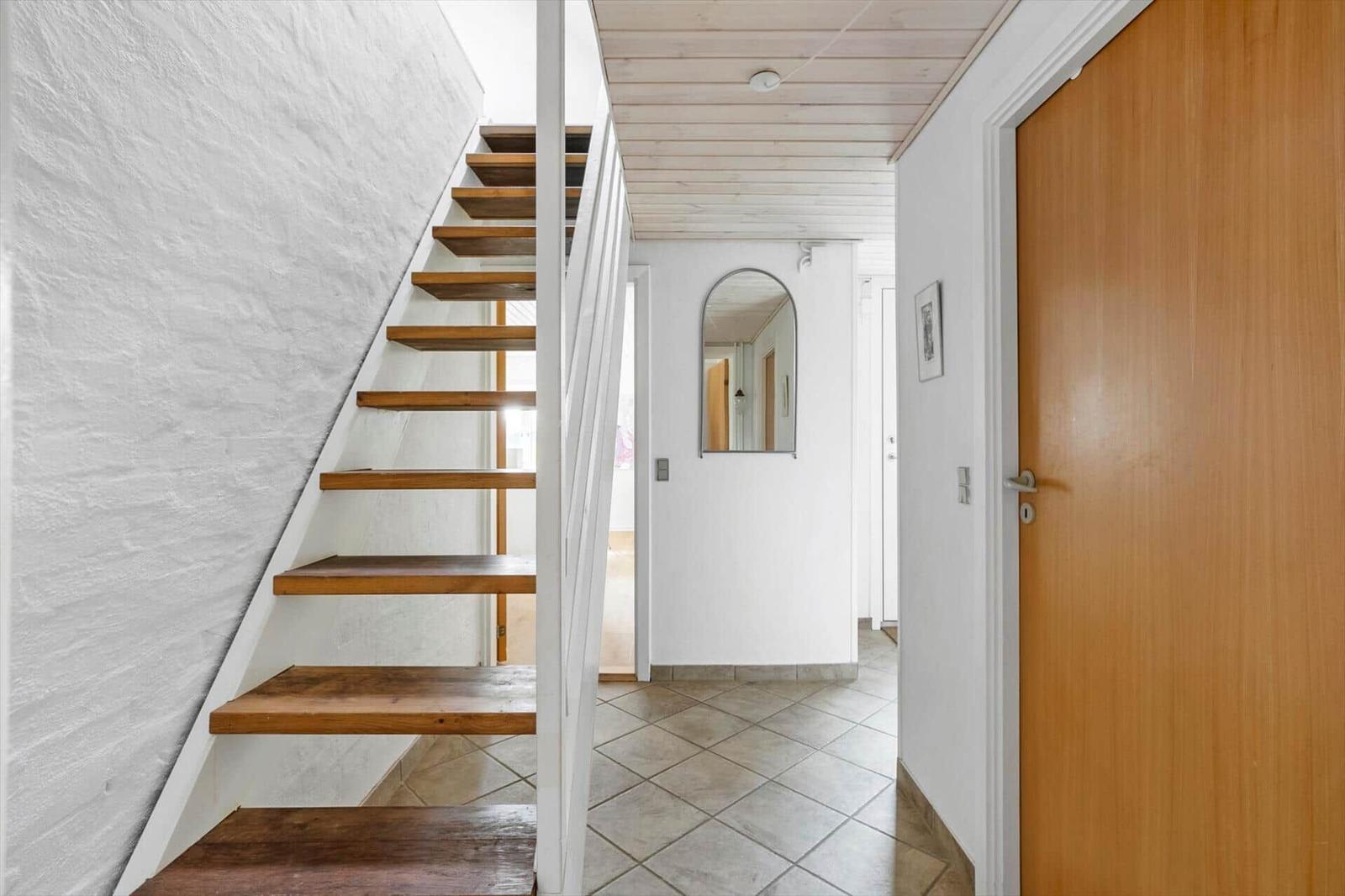 Hallway with wooden staircase, mirror, and wooden door.
