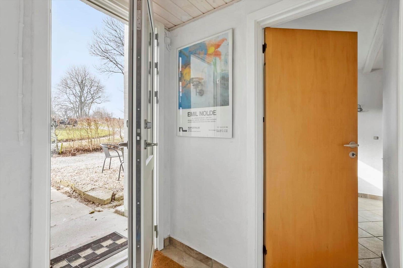 Entrance area with door and poster on the wall. Through the glass door, an outdoor area with a chair is visible.
