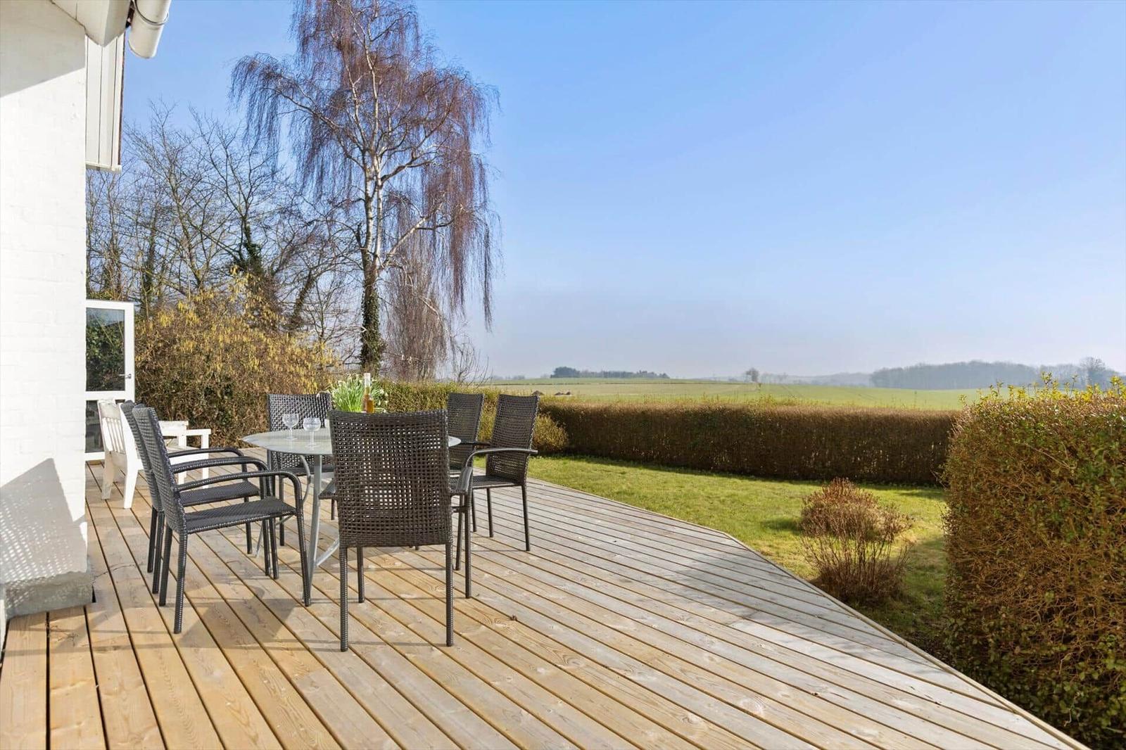 Deck with table and chairs, view of green fields and trees.