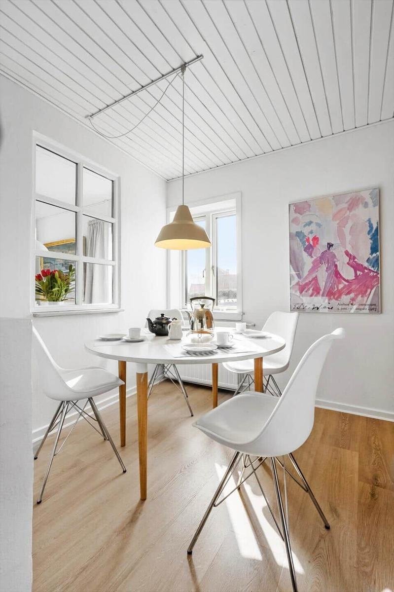 Dining room with round table, white chairs, and wooden floor. A painting hangs on the wall.