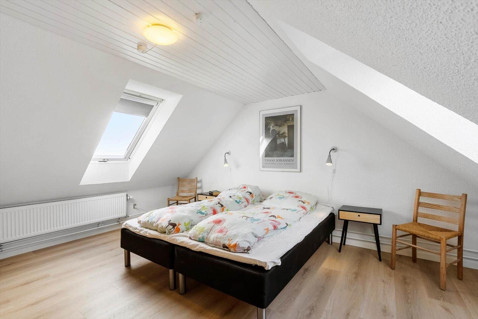Bedroom with skylight, bed, chairs, and bedside table.