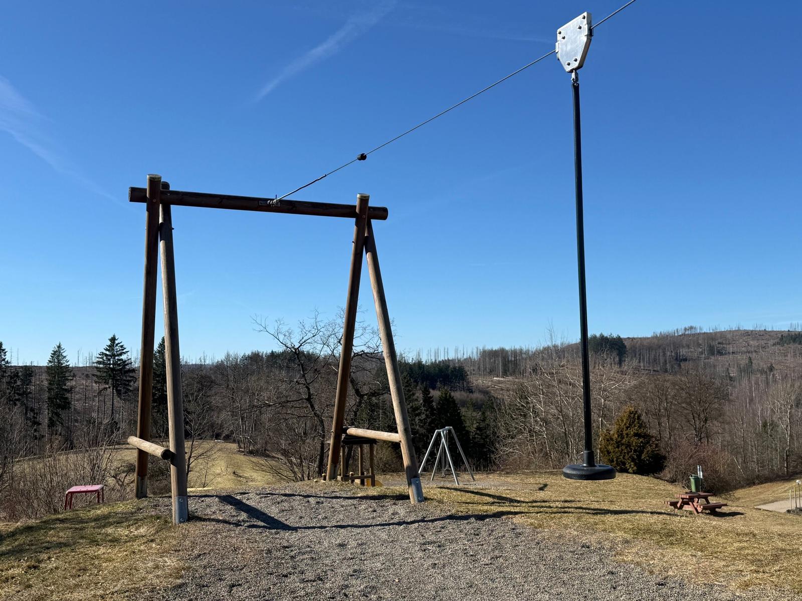 Zugang zum Seilpark mit Holzgerüst und Blick auf bewaldete Hügel.