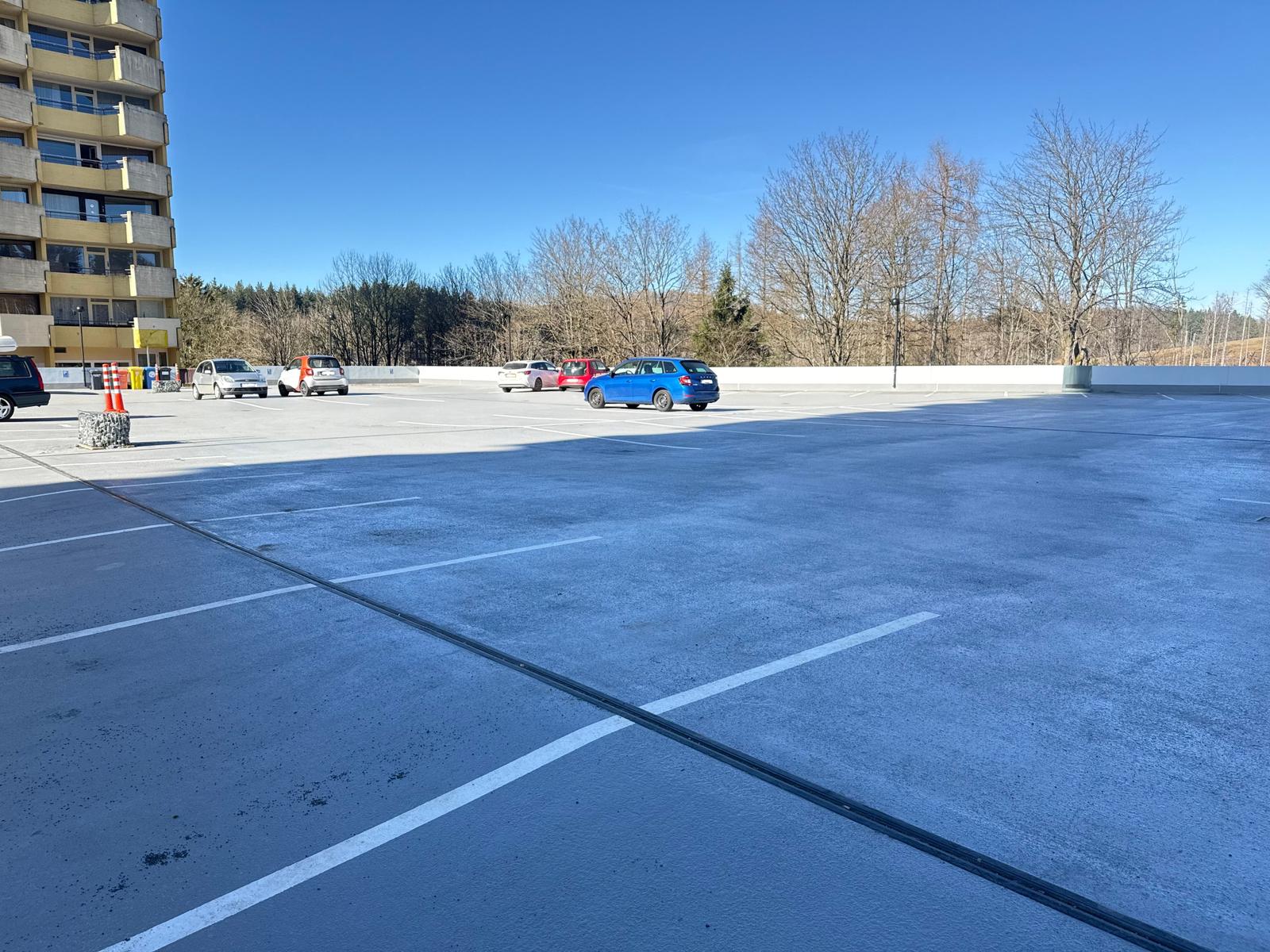Großes Parkplatzareal mit mehreren Autos und Wohngebäude im Hintergrund.