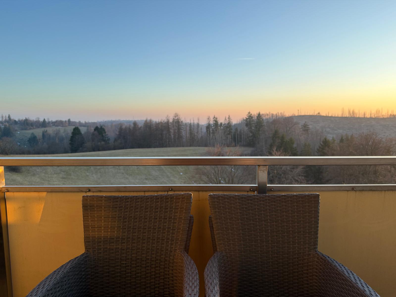 Zwei Stühle auf Balkon mit Blick auf Wald und Hügel bei Sonnenuntergang.