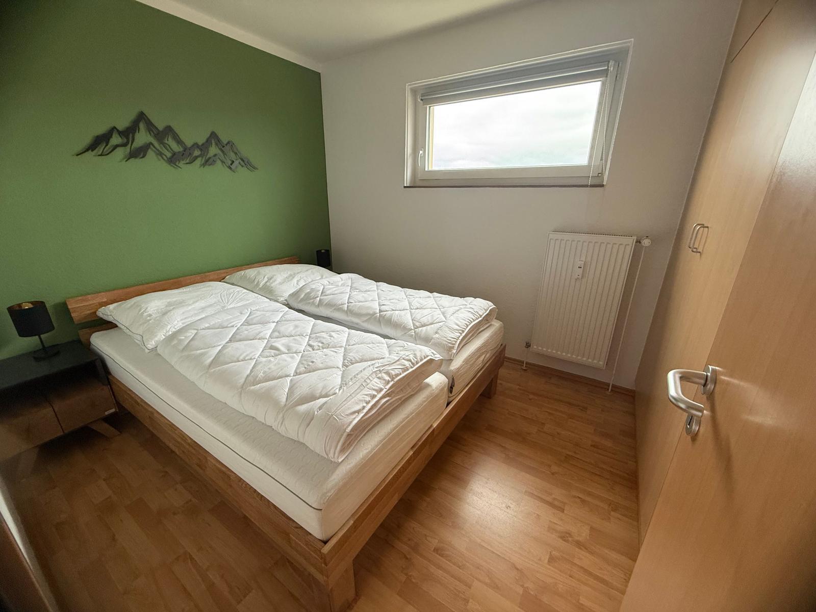 Schlafzimmer mit Doppelbett, grüner Wand und Fenster.