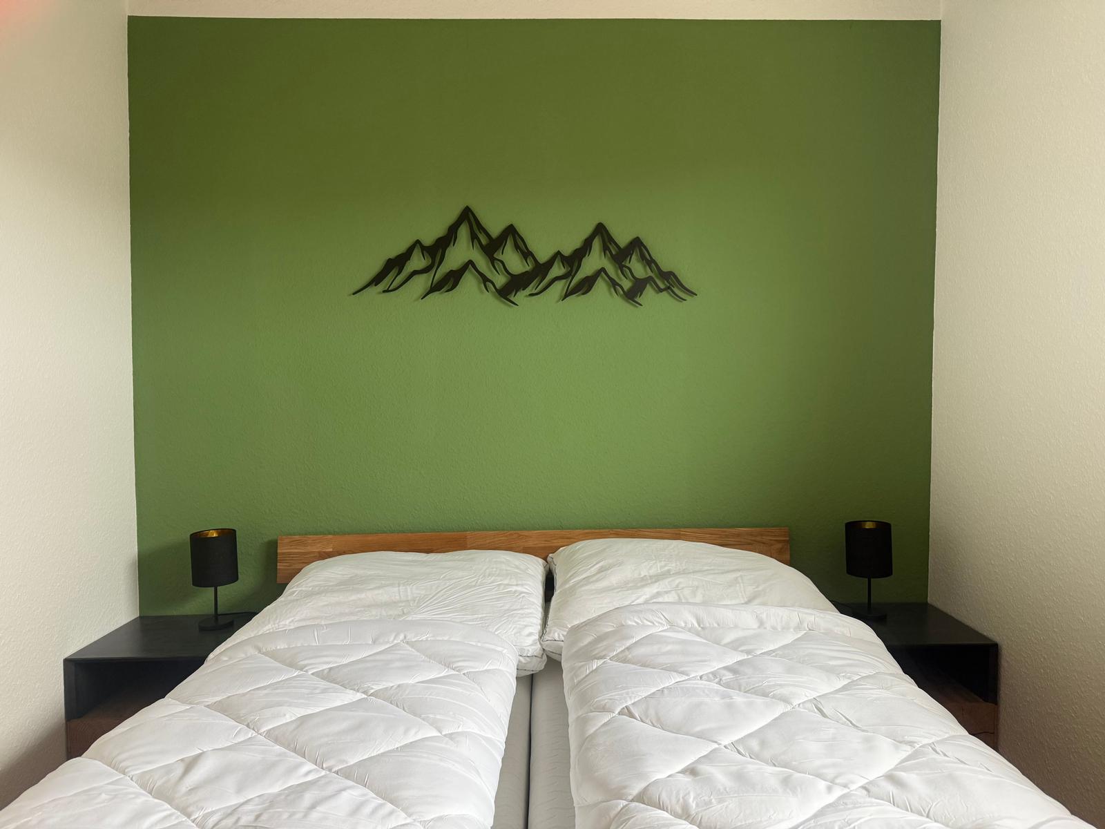 Schlafzimmer mit grüner Wand und Berg-Dekoration über dem Bett.