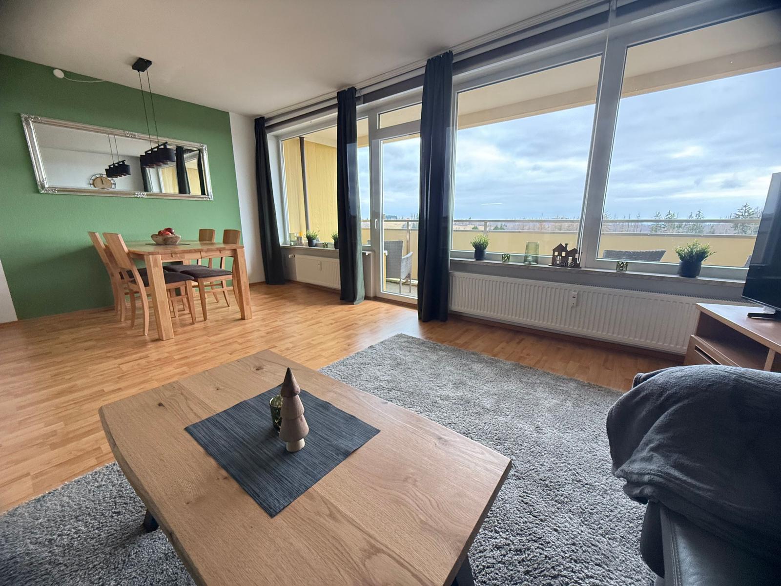 Wohn- und Essbereich mit Balkon, Holzboden und grüner Wand.