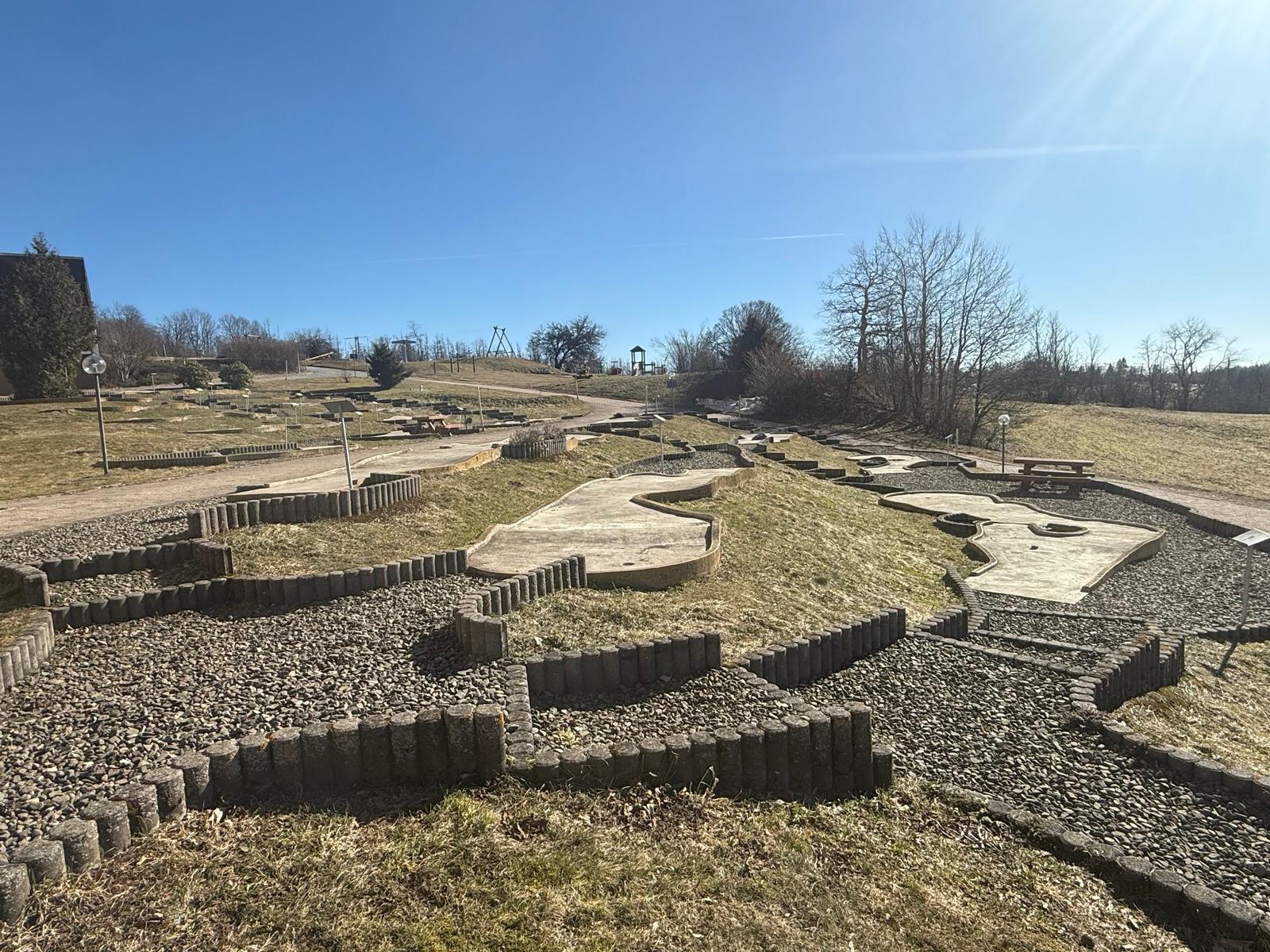Ein Minigolfplatz mit Grasflächen und Kiesbereichen unter blauem Himmel.
